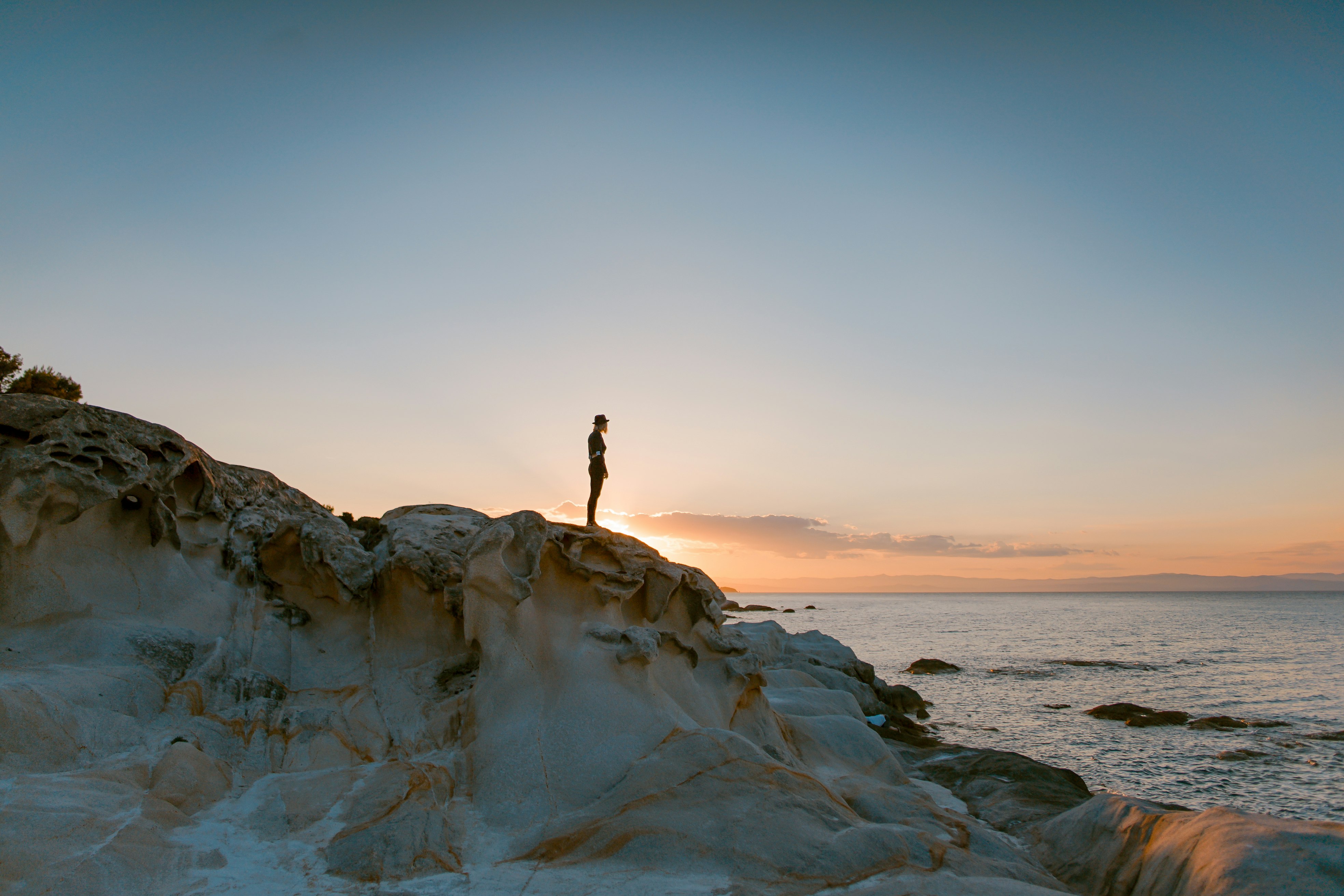 person standing on rock formation beside body of water